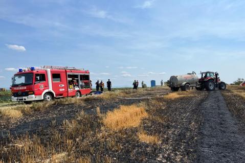 Feuerwehrauto und Traktor mit Güllefass auf einem verbrannten Getreidefeld