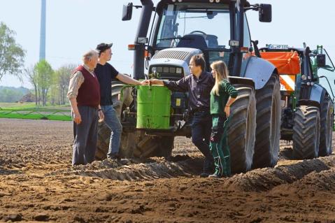 Traktor auf dem Acker mit vier Personen aus der Landwirtschaft drumherum