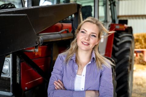 Junge Landwirtin vor einem Traktor stehend