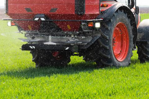 Ein Traktor mit Mineraldüngerstreuer fährt zur Stickstoffdüngung über ein Getreidefeld