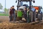 Traktor auf dem Acker mit vier Personen aus der Landwirtschaft drumherum